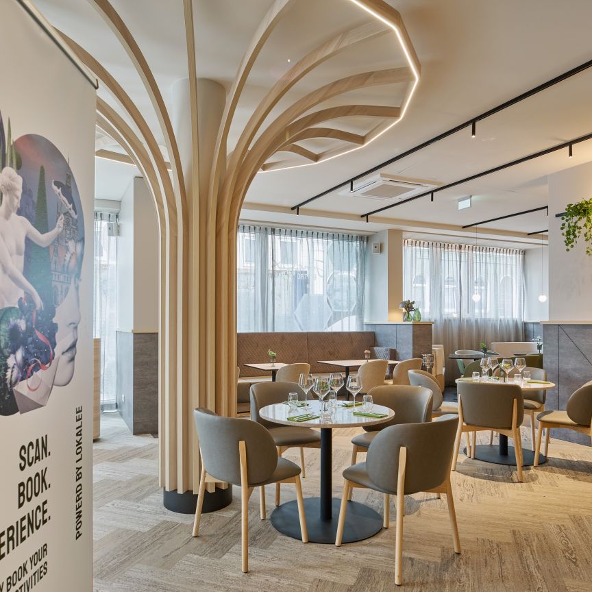 Modernes Hotelrestaurant mit runden Tischen, grauen Stühlen, dekorativen Holzsäulen und einem Banner mit "Hannover" und QR-Code.