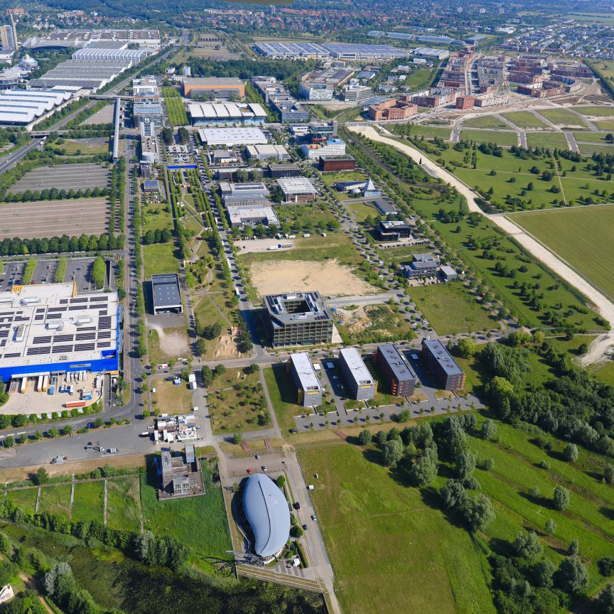 Luftaufnahme eines Industrie- und Gewerbegebiets mit Straßen, Gebäuden, Parkplätzen und umliegenden Grünflächen.