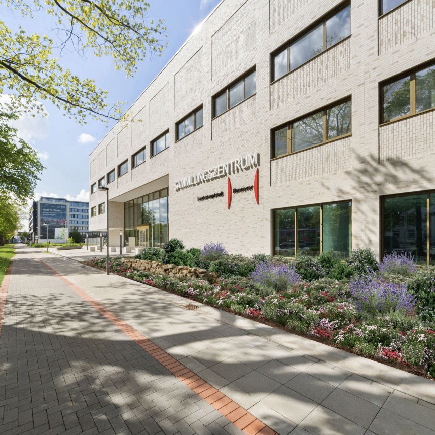 Modernes weißes Bürogebäude mit Aufschrift „Verwaltungszentrum", bepflanztem Vorgarten und gepflastertem Gehweg, Hannover.