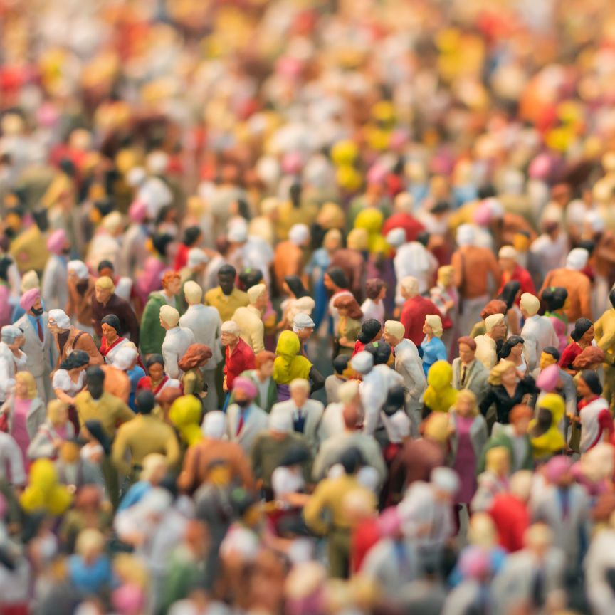 Nahaufnahme vieler bunter Miniaturfiguren, die eine dicht gedrängte Menschenmenge darstellen, mit Tilt-Shift-Effekt.