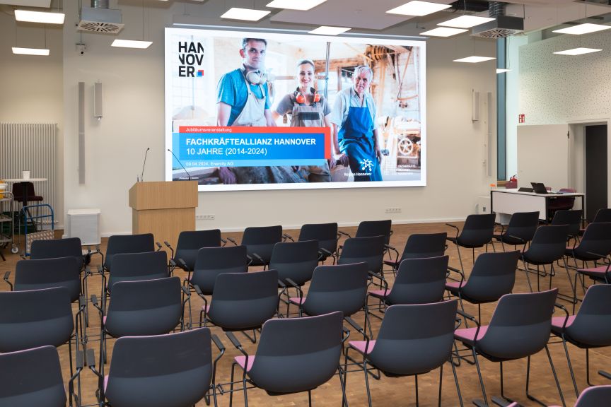 Leerer Konferenzraum mit Stuhlreihen und Leinwand mit Präsentation „Fachkräfteallianz Hannover – 10 Jahre (2014–2024)".