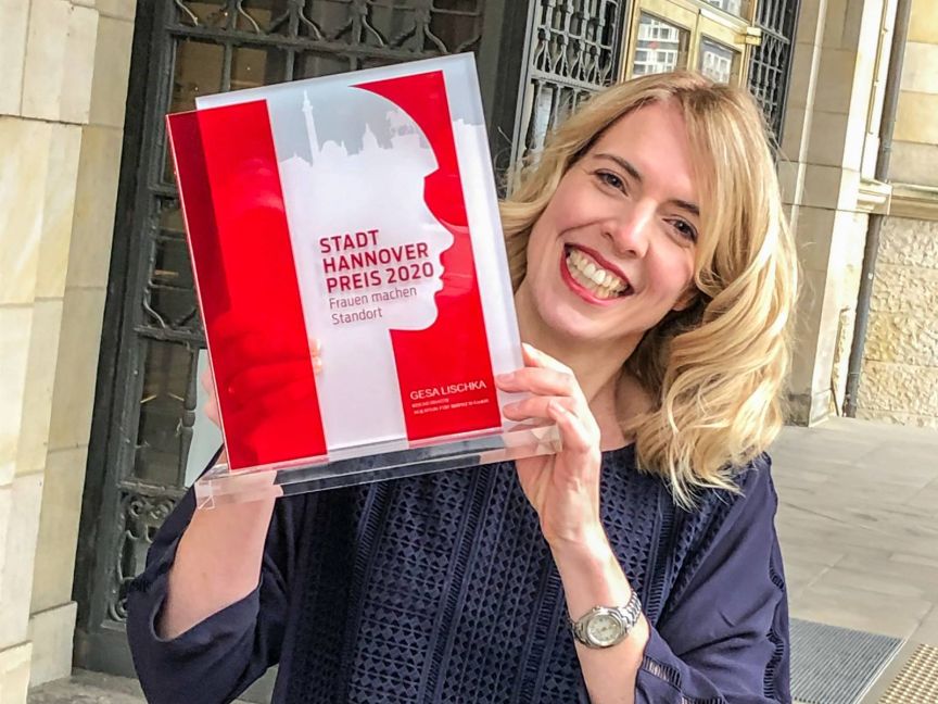 Lächelnde Frau hält Auszeichnung „Stadt Hannover Preis 2020 – Frauen machen Standort" von Gesa Lischka in die Kamera.