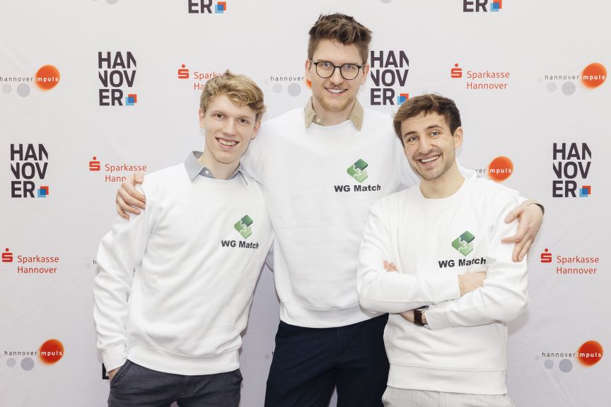 Drei junge Männer in weißen Sweatshirts mit „WG Match"-Logo posieren vor einer Hannover-Sparkasse-Stepandrepeat-Wand.