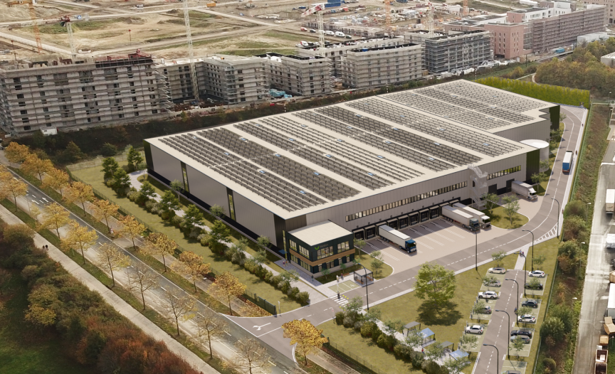 Luftbild eines großen Lagergebäudes mit Solardach, Laderampen, LKW und umliegenden Wohngebäuden im Bau.