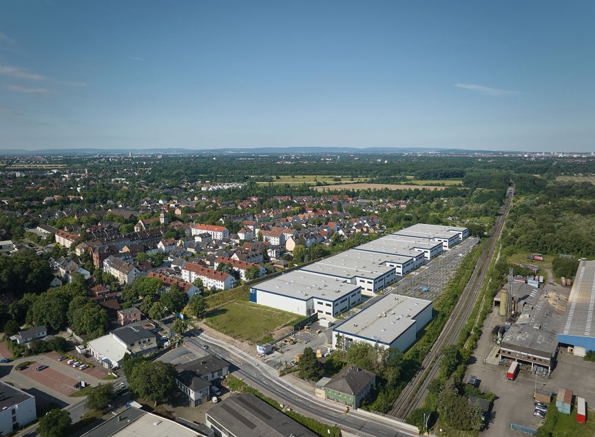 Luftaufnahme einer deutschen Kleinstadt mit Wohnhäusern, Industriegebäuden, Bahngleisen und umliegenden Grünflächen.