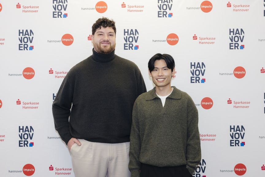 Zwei Männer stehen vor einer Wand mit Logos von Sparkasse Hannover und Hannover Impuls.