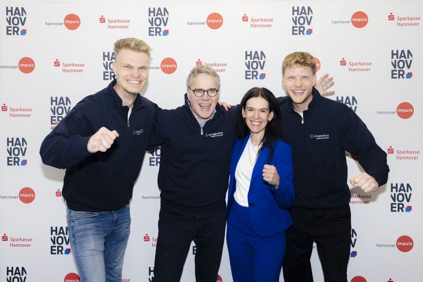 Vier Personen posieren lächelnd vor einer Sponsorenwand mit Logos von Sparkasse Hannover und Hannover Impuls.