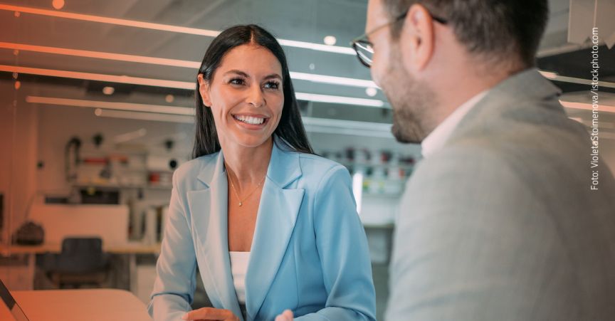 „Zwei Personen in Businesskleidung sitzen sich gegenüber und sprechen miteinander in einem Büro."
