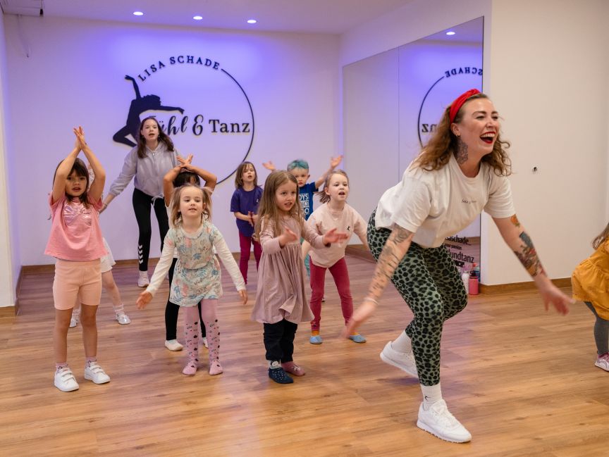 Tanzlehrerin mit Tattoos leitet Kindergruppe in einem Tanzstudio mit Logo „Lisa Schade – Fühl & Tanz".