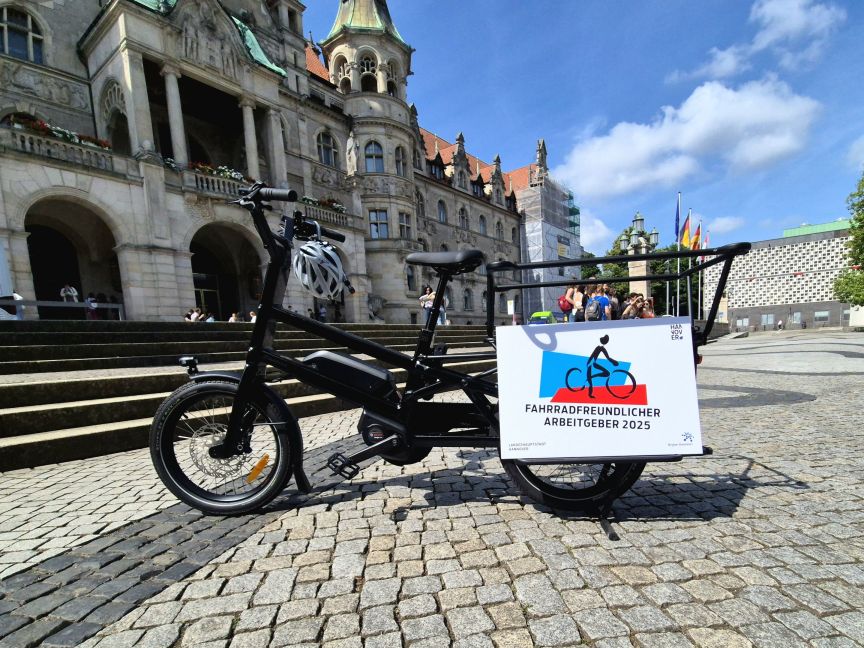 Lastenfahrrad mit Schild „Fahrradfreundlicher Arbeitgeber 2025" auf Kopfsteinpflaster vor historischem Gebäude.