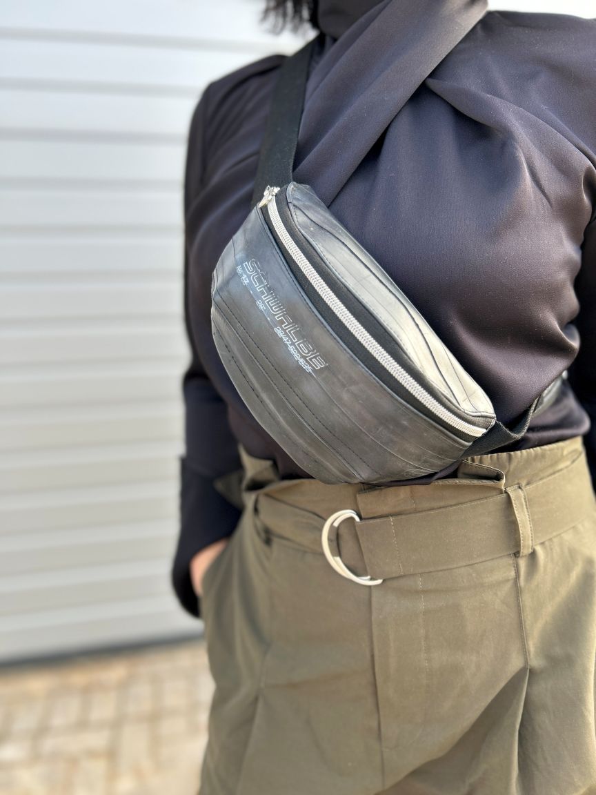 Person in dunklem Oberteil und olivfarbener Hose trägt eine graue Gürteltasche mit Schriftzug "Schwalbe".