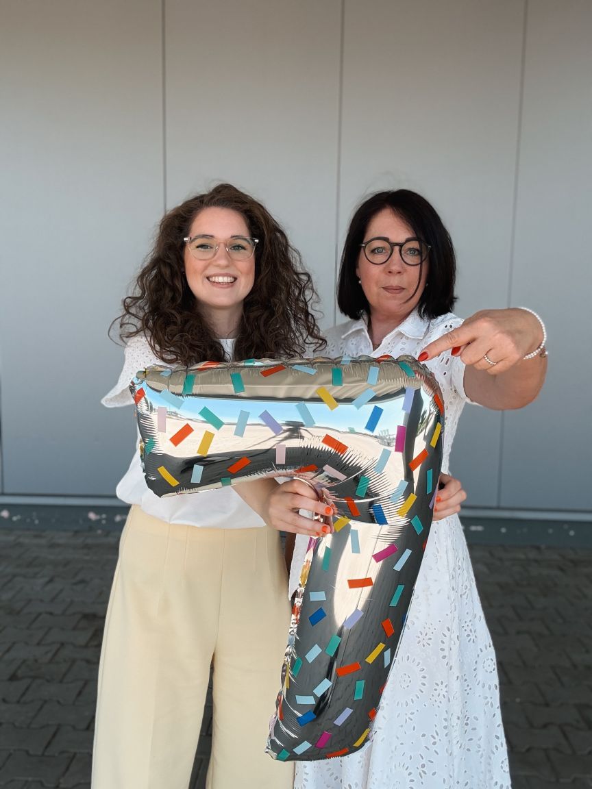 Zwei Frauen mit Brillen halten gemeinsam einen großen, bunten Folienballon in Form einer 7.