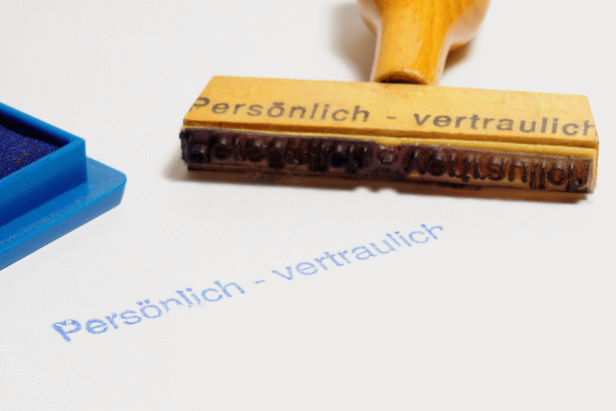 Holzstempel mit Aufdruck „Persönlich – vertraulich", daneben blaues Stempelkissen und Abdruck auf weißem Papier.