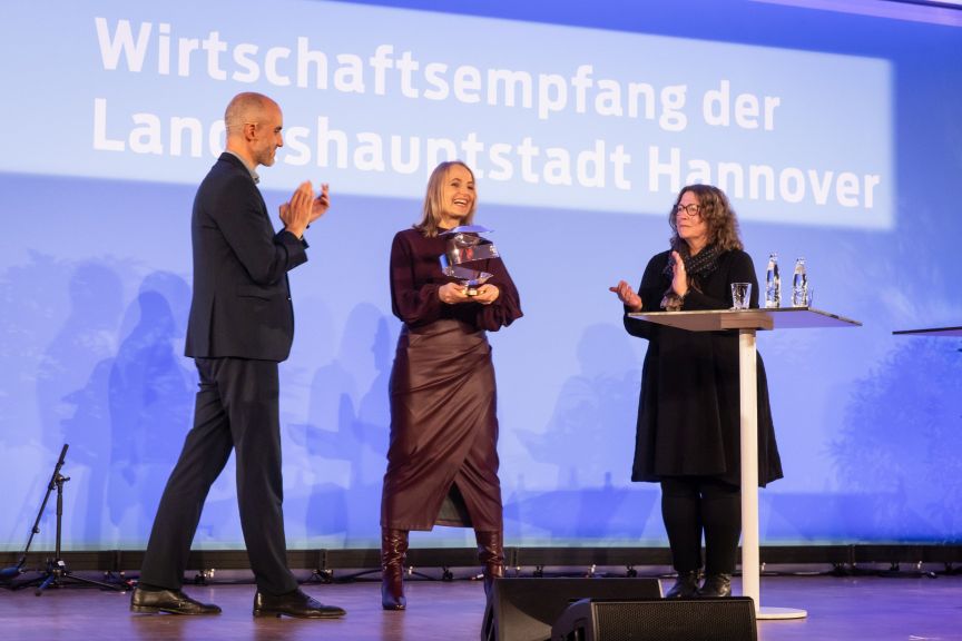 Drei Personen auf einer Bühne beim Wirtschaftsempfang der Landeshauptstadt Hannover; eine Frau hält eine Auszeichnung.