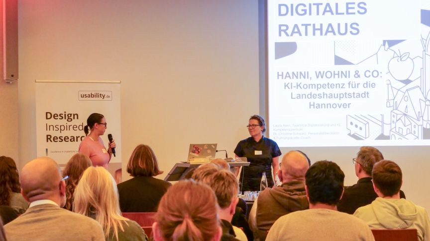 Zwei Personen präsentieren vor Publikum. Leinwand zeigt „Digitales Rathaus – Hanni, Wohni & Co." Banner: usability.de.