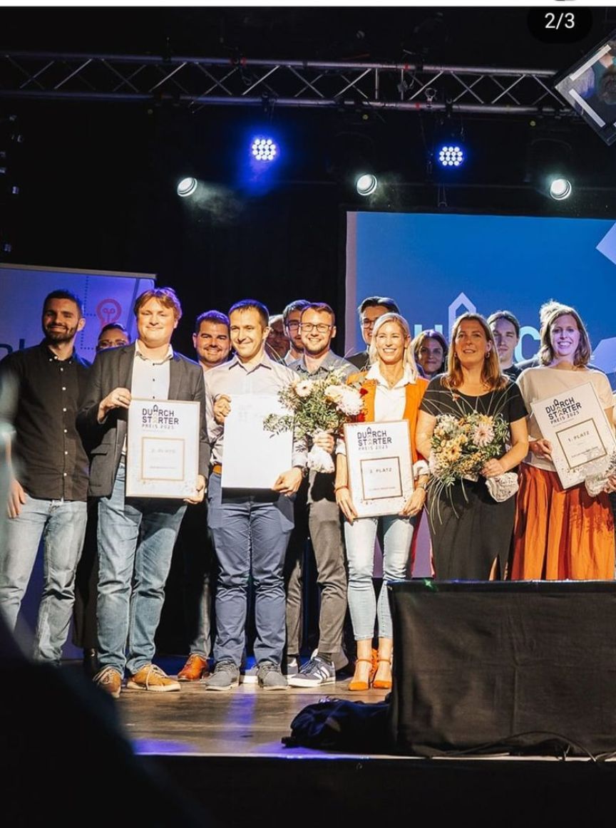 Gruppe von Personen auf einer Bühne, einige halten Urkunden und Blumen bei einer Preisverleihung.