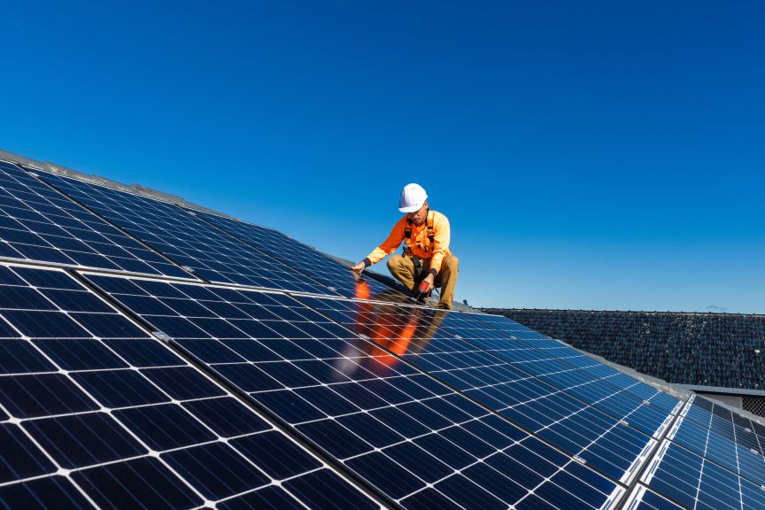 Mann auf einem Dach mit PV-Anlage unter blauem Himmel.