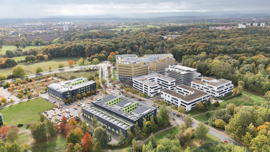 Luftaufnahme eines Bürokomplexes mit mehreren Gebäuden, umgeben von herbstlichem Mischwald und Grünflächen.