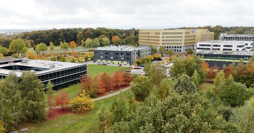 Luftaufnahme eines Campus mit mehreren modernen Gebäuden, umgeben von herbstlich gefärbten Bäumen und Grünflächen.