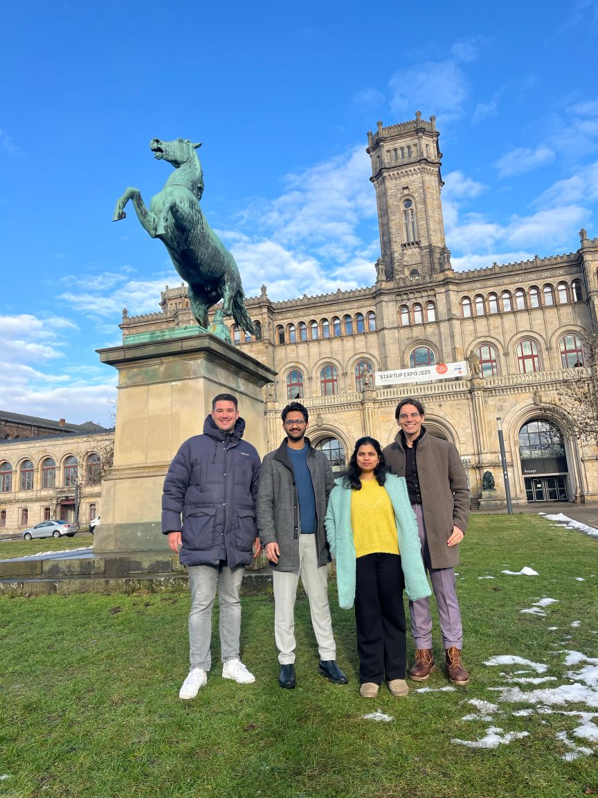 Vier Personen stehen vor einem historischen Gebäude mit einer Bronzepferd-Statue auf einem Sockel.