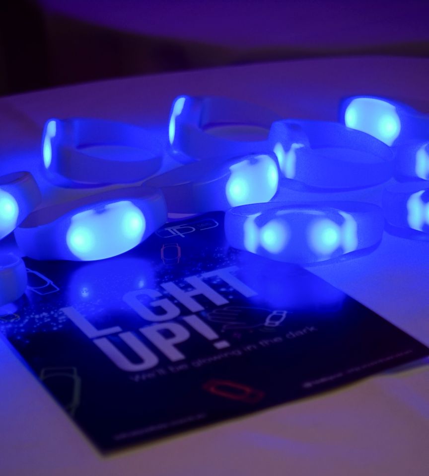 Mehrere leuchtende blaue LED-Armbänder auf einem Tisch, daneben eine Karte mit der Aufschrift „Light Up!".