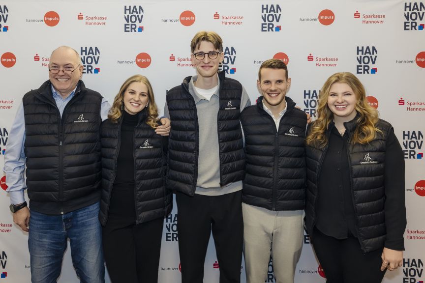 Fünf Personen in schwarzen Westen stehen vor einer Sponsorenwand mit Logos von Sparkasse Hannover und Hannover Impuls.