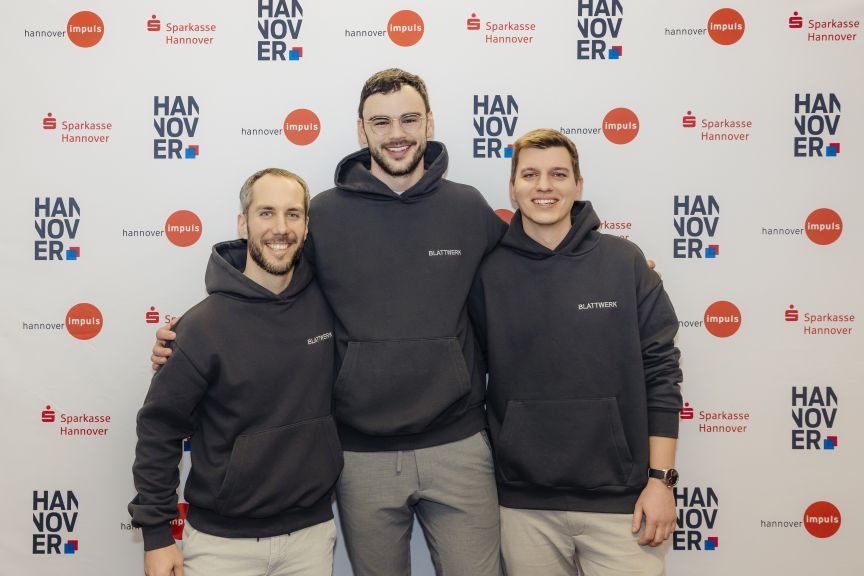 Drei Männer in schwarzen Hoodies vor einer Sponsorenwand mit Logos von Sparkasse Hannover und Hannover Impuls.