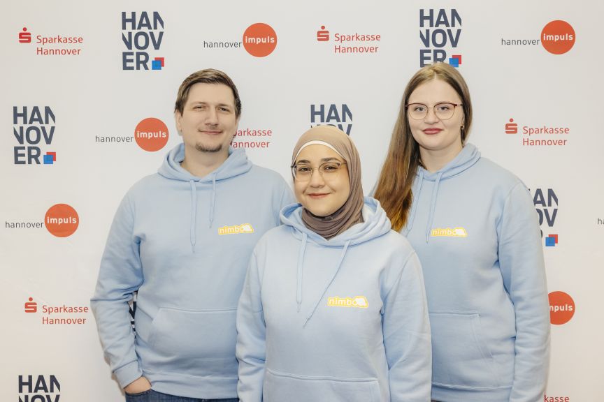 Drei Personen in hellblauen Hoodies vor einer Sponsorenwand mit Logos von Sparkasse Hannover und Hannover Impuls.