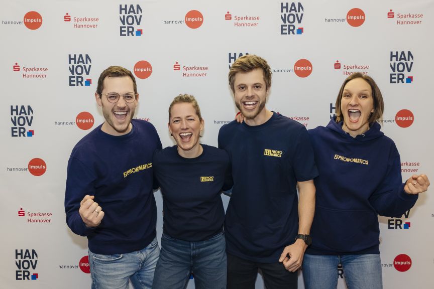 Vier Personen in dunkelblauen Sweatshirts posieren lachend vor einem Sparkasse-Hannover-Banner.