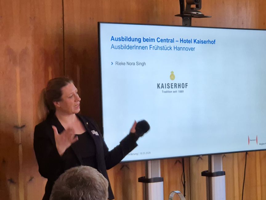Frau präsentiert vor Leinwand mit Folie „Ausbildung beim Central – Hotel Kaiserhof, AusbilderInnen Frühstück Hannover".