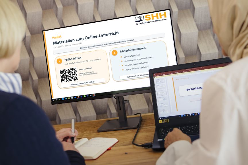 Zwei Personen sitzen vor einem Monitor mit deutschsprachiger Padlet-Präsentation und einem Laptop. Eine Person schreibt in ein Notizbuch.