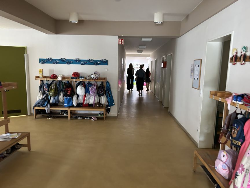 Flur im Kindergarten mit Garderobe und mehreren Personen am Ende vom Gang.