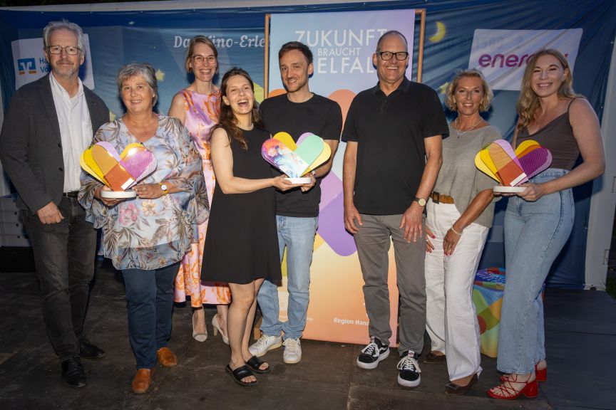 Mehrere Personen freuen sich und halten insgesamt drei Awards in der Hand.