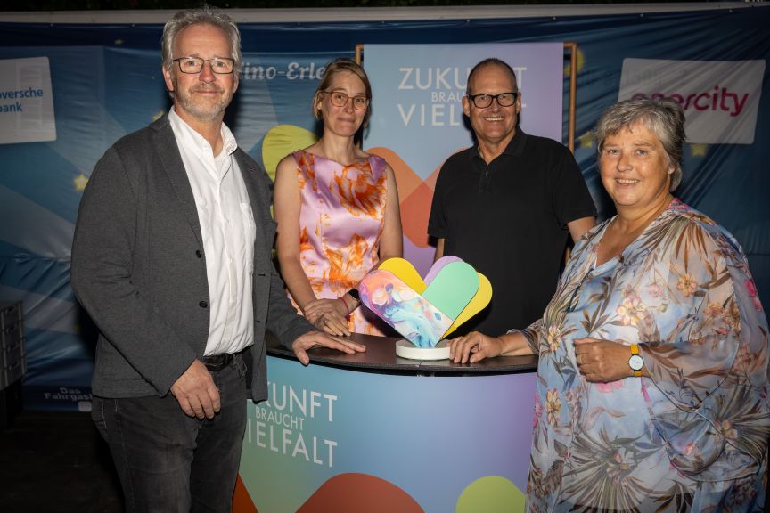 Zwei Frauen und zwei Männer mit dem Preis an einem Tresen mit Logo Zukunft braucht Vielfalt.