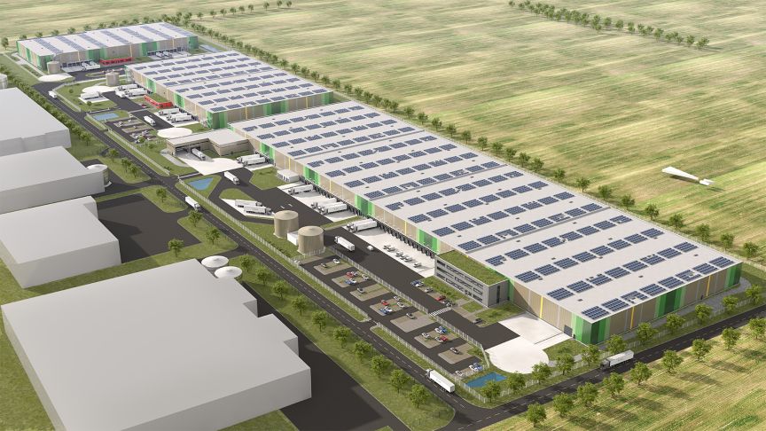 Luftaufnahme eines großen weißen Industriegebäudes mit Solarpanelen auf dem Dach, Parkplatz und umliegenden Feldern.