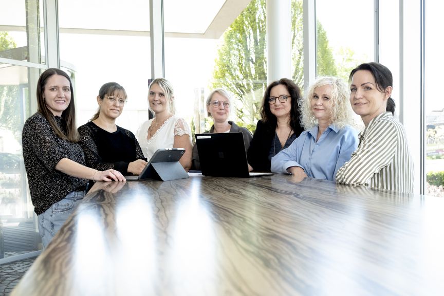 Sieben Frauen stehen nebeneinander und lächeln in die Kamera