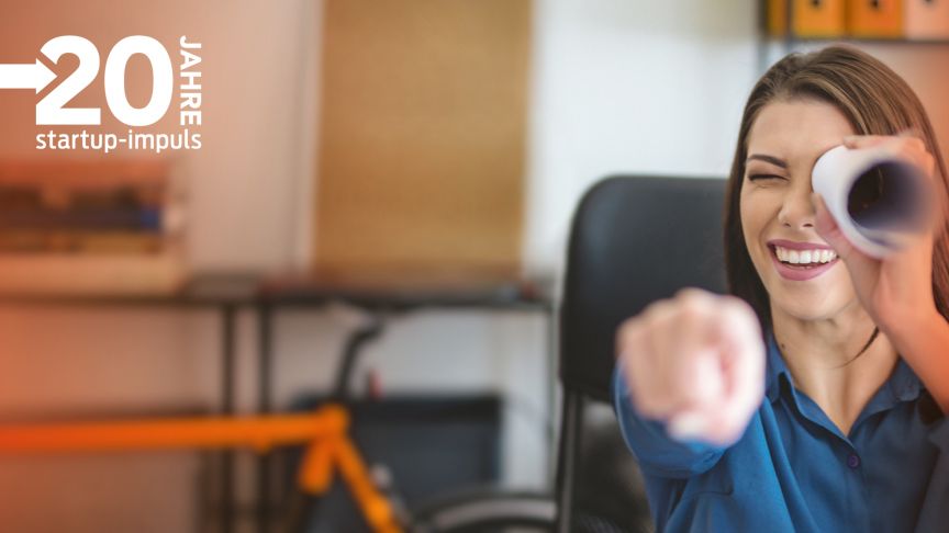 Lachende Frau hält Papierrolle ans Auge und zeigt mit Finger. Logo "20 Jahre startup-impuls" oben links.