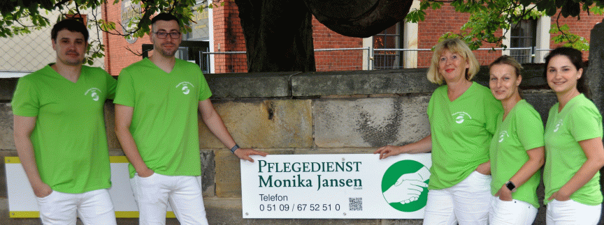 Fünf Personen in grünen T-Shirts und weißen Hosen halten ein Schild mit „Pflegedienst Monika Jansen" vor einem Baum.