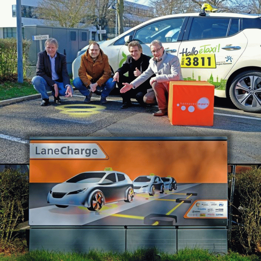Vier Männer kniend vor E-Taxi mit Induktionsladepunkt am Boden; darunter Infotafel zum „LaneCharge"-System.