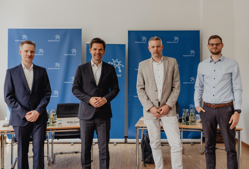 Vier Männer stehen vor blauen Rollup-Bannern mit der Aufschrift „Region Hannover" in einem Besprechungsraum.