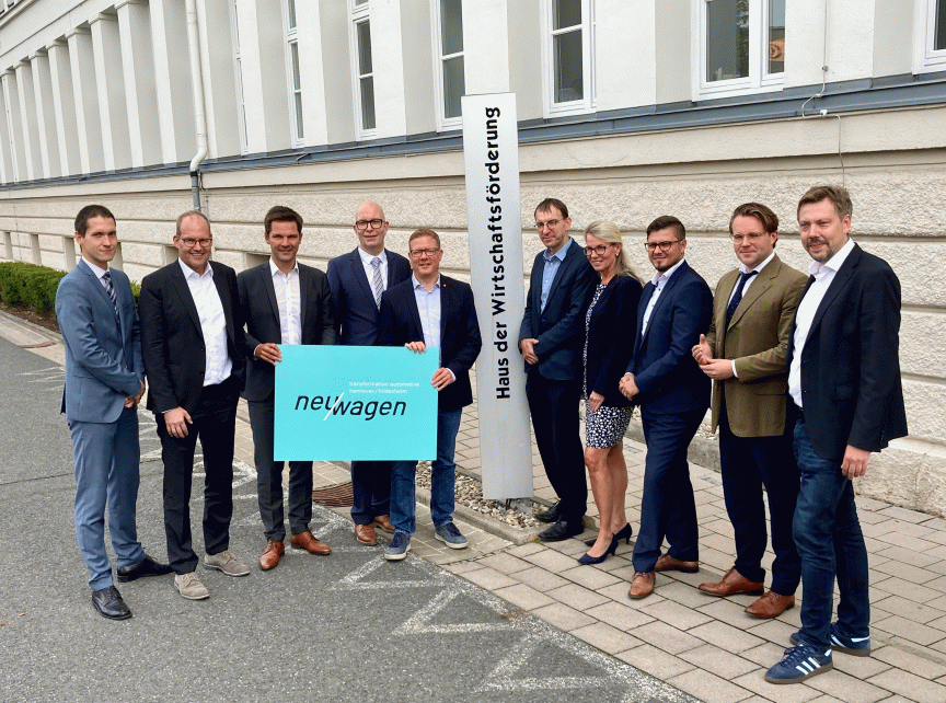 Gruppe von 10 Personen vor einem Gebäude mit Schild „Haus der Wirtschaftsförderung", eine Person hält „neuwagen"-Logo.
