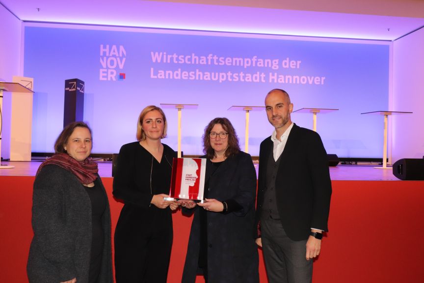 Vier Personen stehen vor einer Leinwand mit „Wirtschaftsempfang der Landeshauptstadt Hannover", zwei halten eine Auszeichnung.