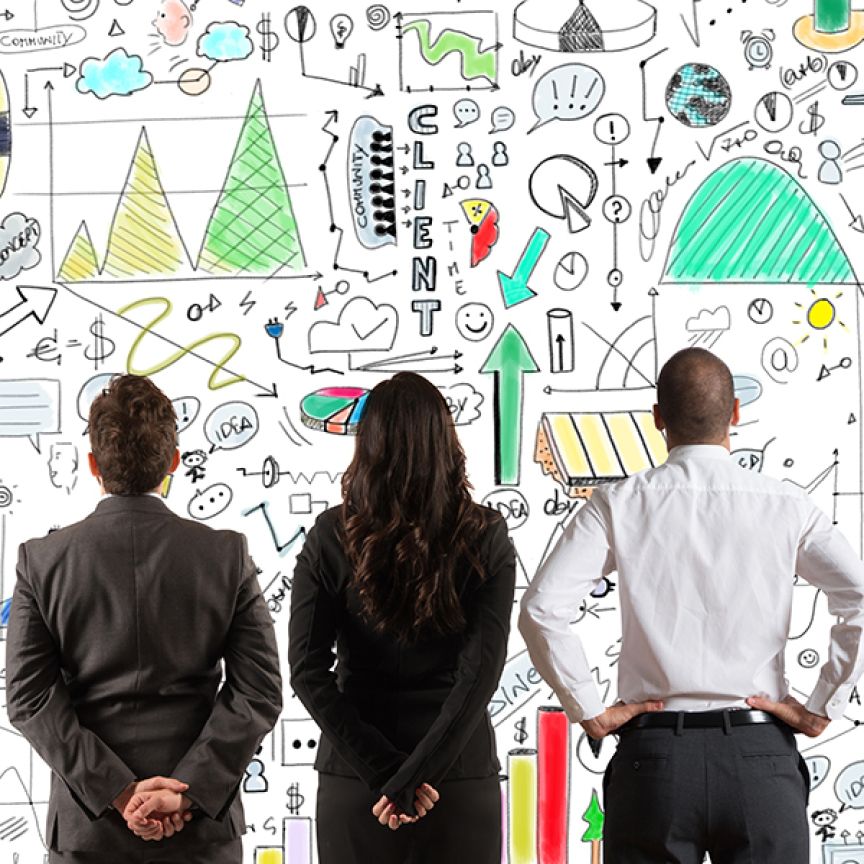 Drei Personen in Businesskleidung stehen vor einer weißen Wand mit bunten Diagrammen, Pfeilen und Symbolen.