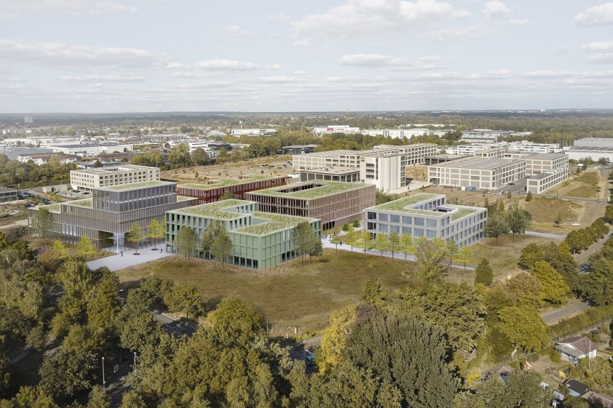 Luftaufnahme eines modernen Bürokomplexes mit Grünflächen und Bäumen, umgeben von weiteren Gebäuden und Straßen.