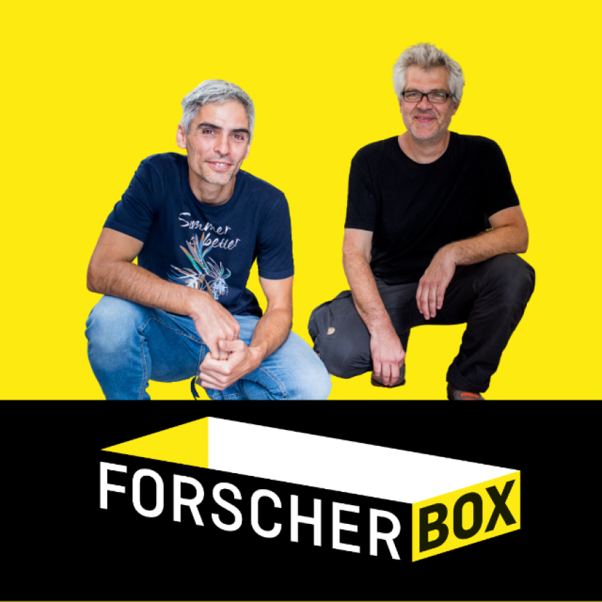 Zwei Männer hocken vor gelbem Hintergrund, darunter schwarzes Logo mit Text „Forscher Box".