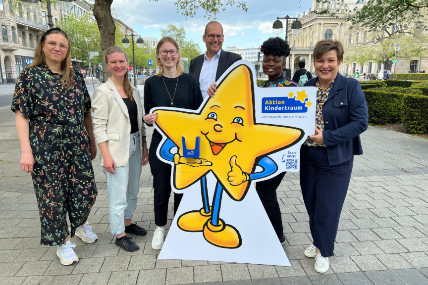 Sechs Personen posieren mit einem großen Pappaufsteller einer lächelnden Stern-Figur mit "Aktion Kindertraum"-Logo.