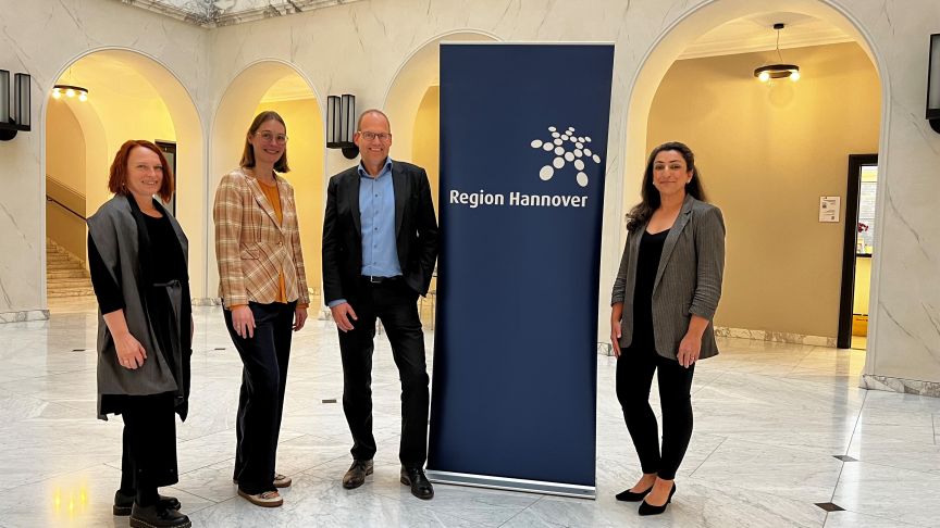 Vier Personen stehen in einem Foyer neben einem Banner mit der Aufschrift „Region Hannover".