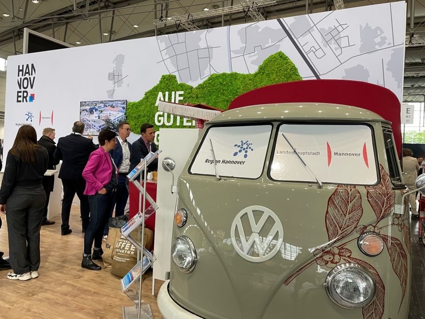 VW-Bus mit Logos „Region Hannover" und „Landeshauptstadt Hannover" vor Messestand mit Hannover-Schriftzug.