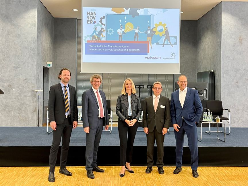 Fünf Personen in Businesskleidung stehen vor einer Präsentationsleinwand mit VDI/VDE-Logo in einem Konferenzsaal.