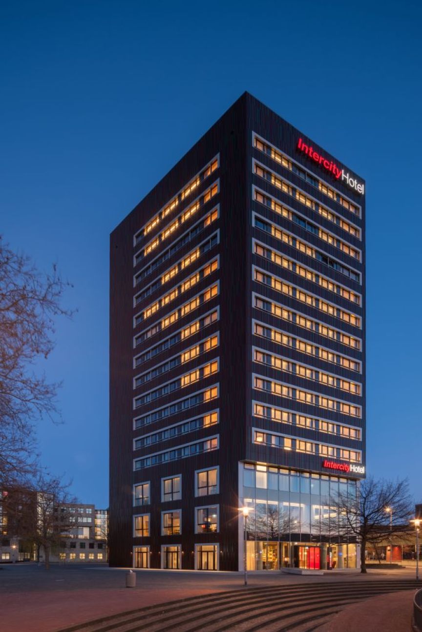 Modernes IntercityHotel-Hochhaus mit beleuchteten Fenstern in der Abenddämmerung, umgeben von einem gepflasterten Platz.